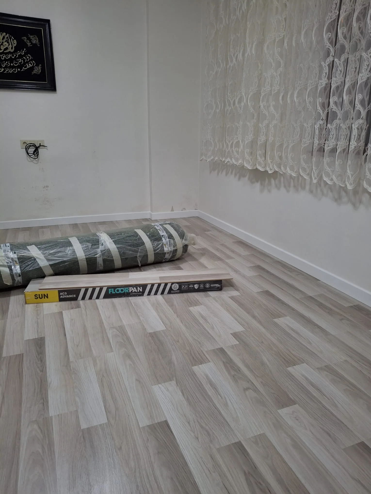 Geniş pencere ışığı altında montajı tamamlanmış açık meşe laminat parke yüzeyi